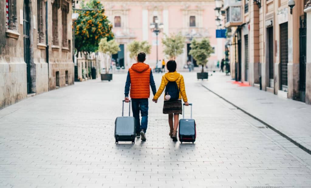 William Russell Blog What is an expat banner couple moving abroad walking with suitcases e1612530695191